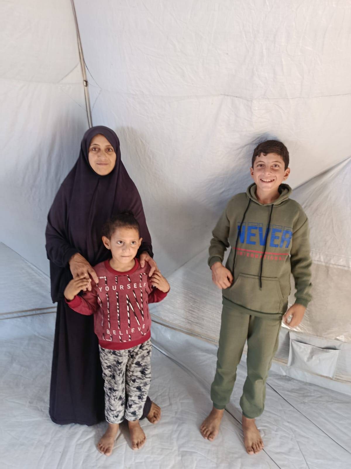 A woman and two children standing together inside a tent