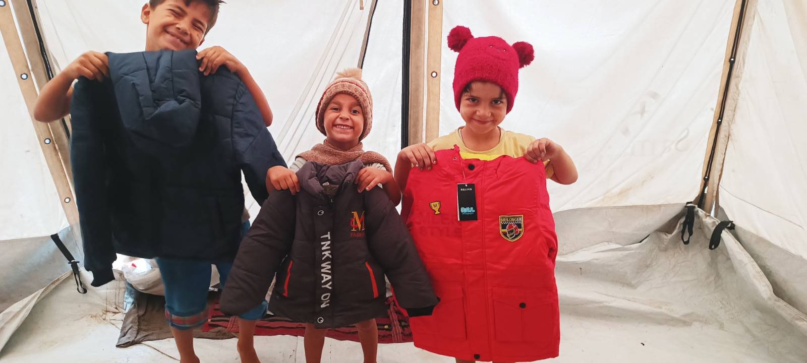 Saam’s three children together inside their tent, holding up winter coats