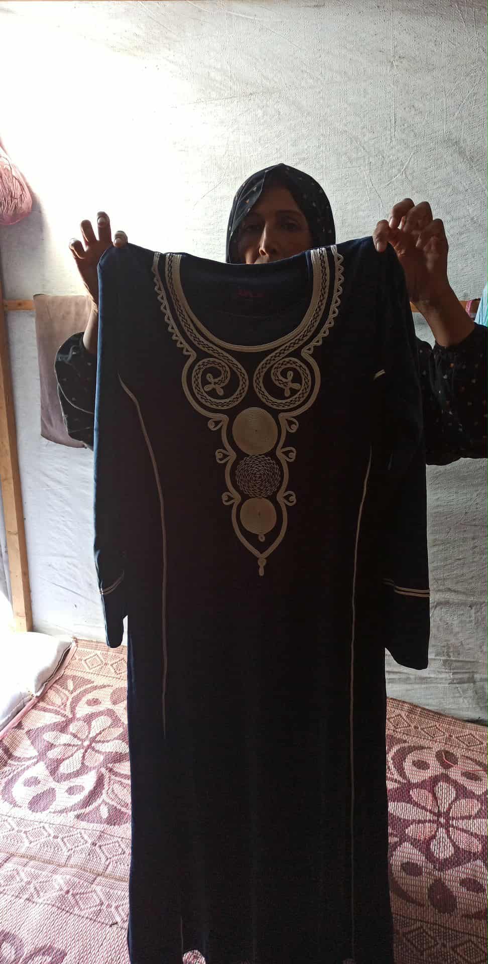 A woman holding up a long embroidered garment inside a tent
